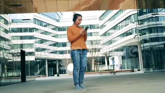 带着女士耳机使用手机的现代城市地区视频的预览图