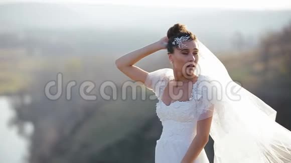 美丽的新娘穿着豪华的白色礼服站在风清秋的荒芜的田野里向她挥动面纱视频的预览图