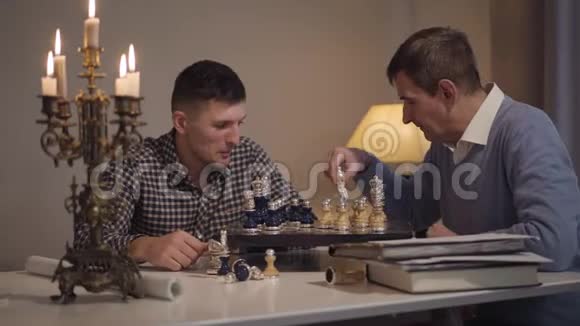 性格开朗的白种人儿子和父亲晚上在家下棋成年男子在室内自由活动视频的预览图