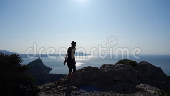 远距离拍摄一名游客女孩她走在悬崖顶上停下来高兴地举起双手慢动作视频的预览图