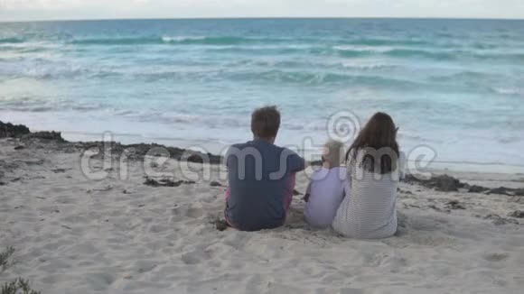 爸爸妈妈和儿子坐在海滩上看海洋视频的预览图