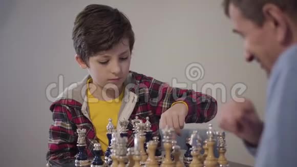 集中的白人男孩下棋和显示胜利姿态的肖像他模糊的祖父视频的预览图