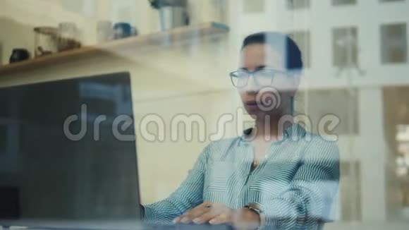 在笔记本电脑上工作的商务女士是通过窗户拍摄的视频的预览图