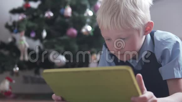 一个金发男孩放学前在家玩平板电脑视频的预览图