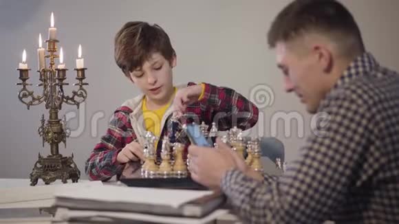 注意力从一个白人小男孩下国际象棋用智能手机和年轻的父亲聊天开始转变起源视频的预览图