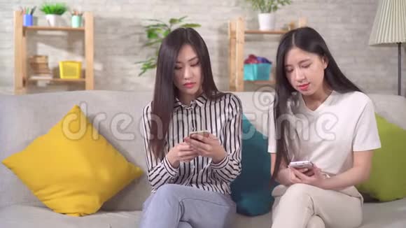 两个快乐的亚洲女孩在客厅沙发上放着智能手机视频的预览图