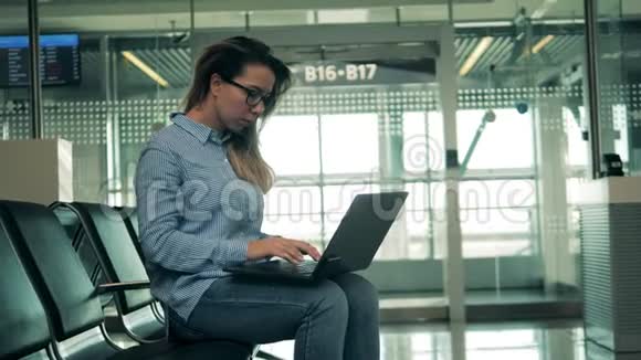 一位戴眼镜的妇女正在机场大厅浏览笔记本电脑视频的预览图