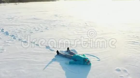 一个女孩在森林的空地上做一个雪天使的身影一个女孩躺在雪地里的空中摄影视频的预览图