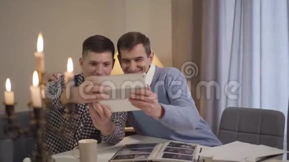 白种人成年父子在平板电脑上拥抱和自拍的肖像快乐的中年男人和快乐的男人视频的预览图