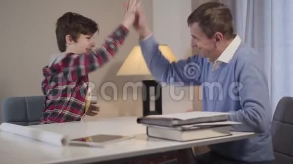 积极的白人小男孩和中年男子给予高五和微笑可爱的孙子和快乐的祖父视频的预览图