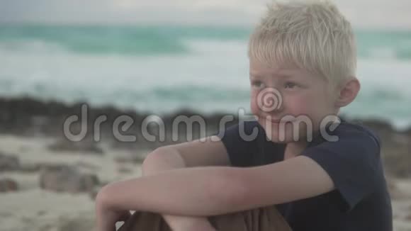 有雀斑的漂亮男孩坐在沙滩上思考视频的预览图