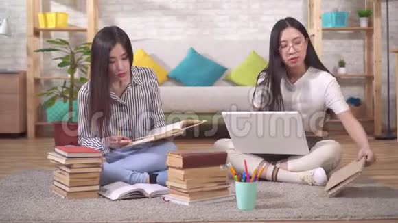 两个可爱的亚洲学生正坐在书和笔记本电脑旁边的地板上准备考试视频的预览图