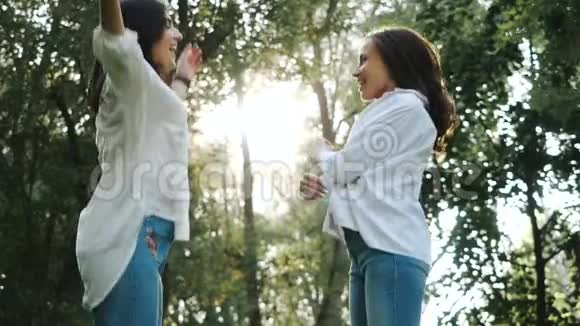 侧面观看两位迷人的年轻女性跳跃和互相看着创造出一张壮观的照片快乐的春天视频的预览图