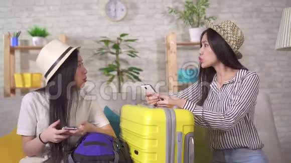 两个失望的亚洲年轻女子坐在客厅里提着手提箱度假视频的预览图