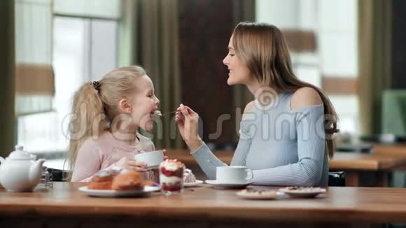 微笑照顾年轻母亲喂养可爱的女儿甜点在咖啡馆吃早餐中型摄影机视频的预览图