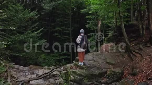 红发女游客背着背包站在瀑布的悬崖边对着一片雾蒙蒙的森林鸟瞰图视频的预览图
