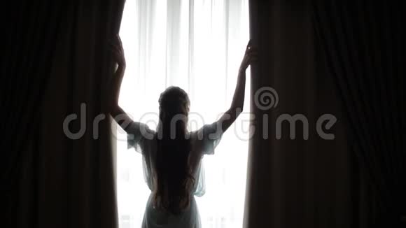 一个年轻的长发的女人把手放在卧室的窗帘上挡住了晨光视频的预览图