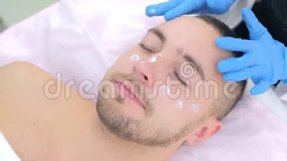 戴手套的美容师正在给顾客的面部按摩皮肤霜视频的预览图