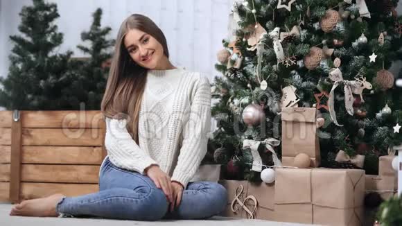 美丽舒适的女孩穿着休闲服装坐在装饰圣诞树附近红色相机宽镜头视频的预览图