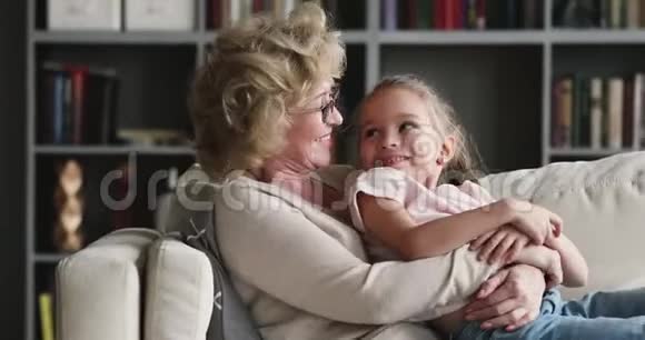 快乐轻松的老奶奶拥抱学龄前孙女休息沙发视频的预览图