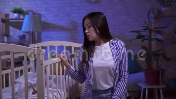 疲惫悲伤的年轻亚洲妈妈摇着婴儿床视频的预览图