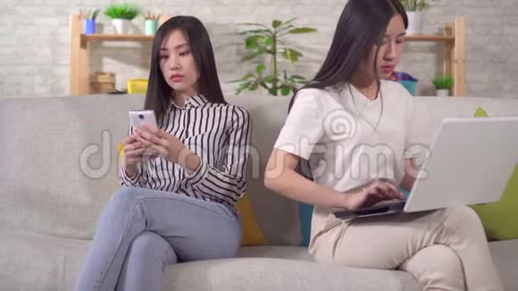两位年轻的亚洲女性正在使用坐在沙发上的小玩意视频的预览图