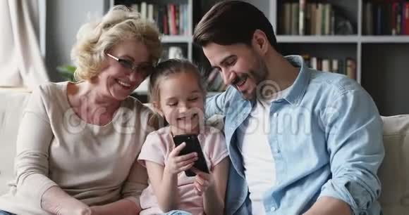 幸福的多代家庭使用智能手机小工具坐在沙发上视频的预览图