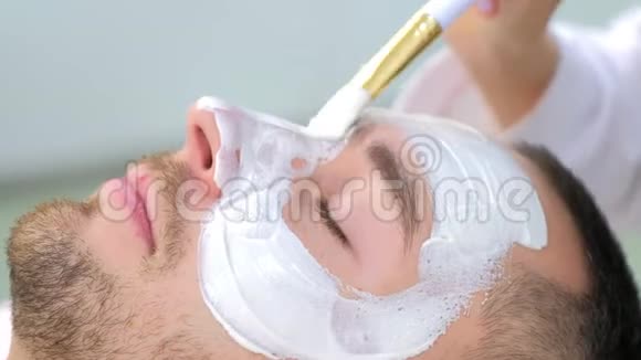 美容师正在用刷子人脸上涂白色保湿面膜视频的预览图