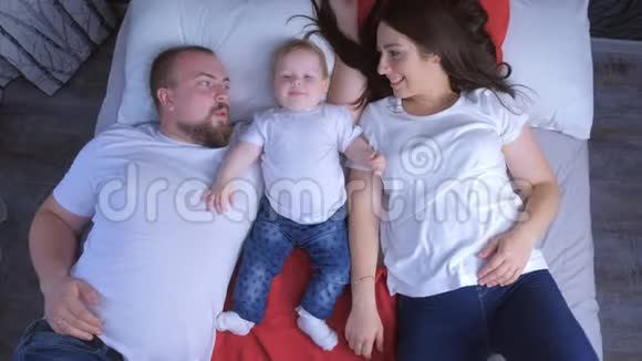 家庭肖像的妈妈爸爸和宝宝躺在床上在家里俯视图视频的预览图