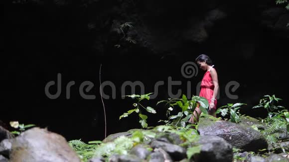 穿着红色衣服的女人独自走在丛林里潮湿狭窄的黑暗峡谷里视频的预览图