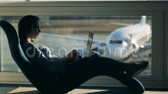 机场休息室一位女士坐在扶手椅上浏览她的笔记本电脑视频的预览图