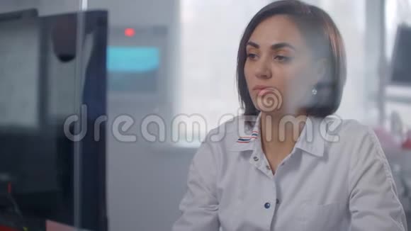 一位穿着白色外套的女医生看着坐在玻璃墙后面明亮办公室里的监视器屏幕现代诊所视频的预览图