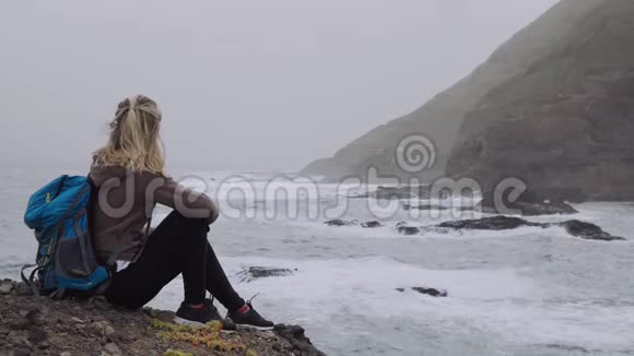 旅游女性欣赏强烈的波浪溅入岩石海岸线巨大的火山山脉崎岖的跋涉视频的预览图