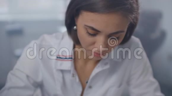 一位女医生坐在桌子旁用钢笔写处方给一个病人在玻璃墙后面视频的预览图