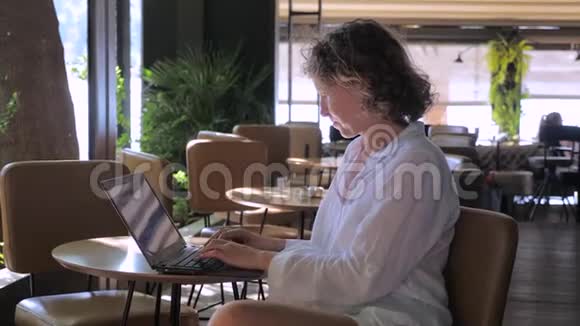 穿白色衣服的女人在咖啡馆里用笔记本电脑工作旅行时工作商业女性搜索信息更新视频的预览图