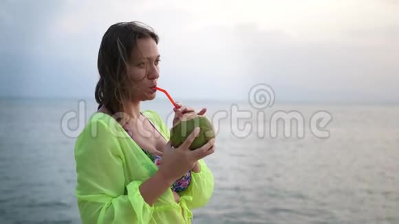 黑色素瘤成年女性手表海景和享受饮用新鲜果汁从椰子视频的预览图