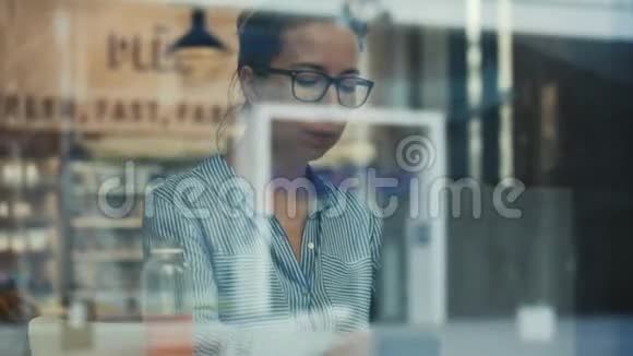 一个戴眼镜的女人用手提电脑通过玻璃拍摄视频的预览图