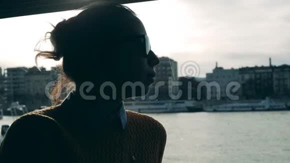 戴墨镜的女人骑着船沿着城市的河流视频的预览图