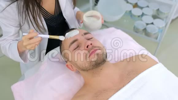 美容师正在用刷子人脸上涂白色保湿面膜视频的预览图
