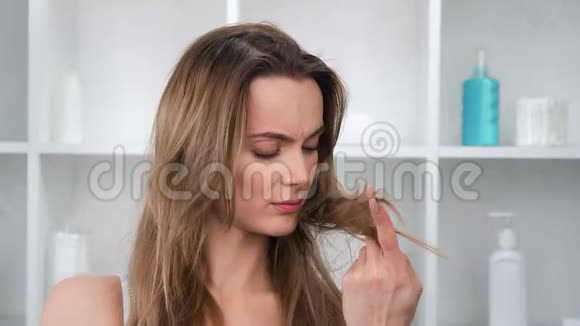 在浴室4k镜头拍摄的令人沮丧的美丽女人触摸糟糕状况的头发的特写照片视频的预览图