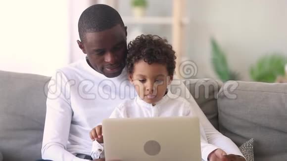 年轻的非洲爸爸教专注的孩子儿子用笔记本电脑视频的预览图
