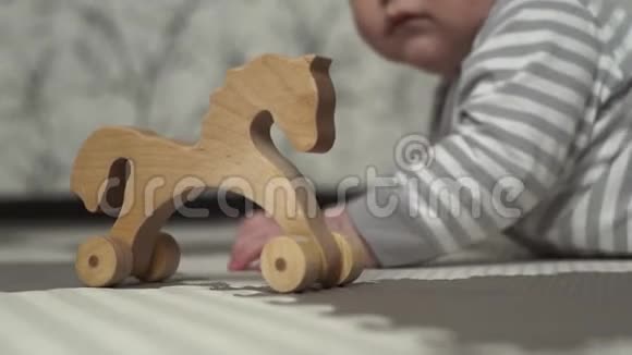 木制玩具马站在地板上背景中一个穿着灰白色条纹睡衣的小孩子正在玩耍视频的预览图