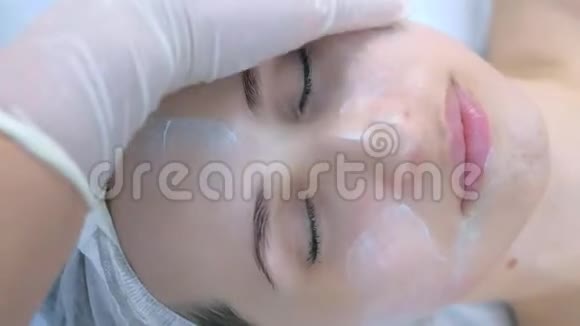 戴手套的美容师正在给客户的面部按摩皮肤涂上奶油视频的预览图