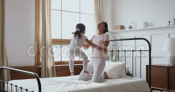 无忧无虑的亚洲小女儿在床上蹦蹦跳跳地和妈妈玩耍视频的预览图