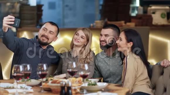 两对快乐的夫妇自拍使用智能手机一起在晚餐4k龙红相机视频的预览图