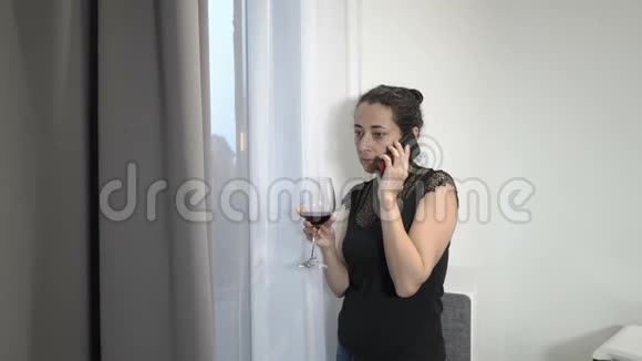 一个漂亮的成年女孩一个商务小姐正在房间的窗户边打电话拿着一杯红酒视频的预览图