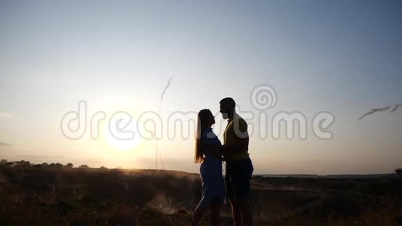 年轻漂亮的情侣女孩和男孩在夕阳背景下在田野上调情一个女孩和一个男人相爱视频的预览图
