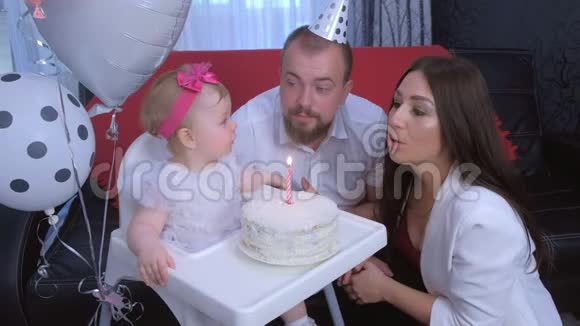 家庭肖像妈妈爸爸在小女孩的第一个生日吹蜡烛视频的预览图