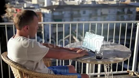 年轻的男性自由职业者正坐在阳台上用笔记本电脑工作视频的预览图