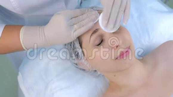 美容师在美容诊所用棉垫擦拭女人脸特写视频的预览图